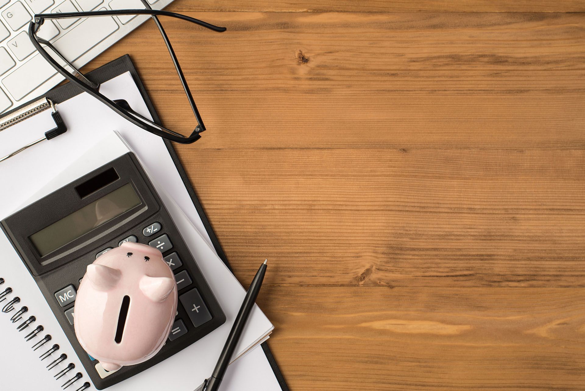 A piggy bank is sitting on top of a calculator on a wooden desk.