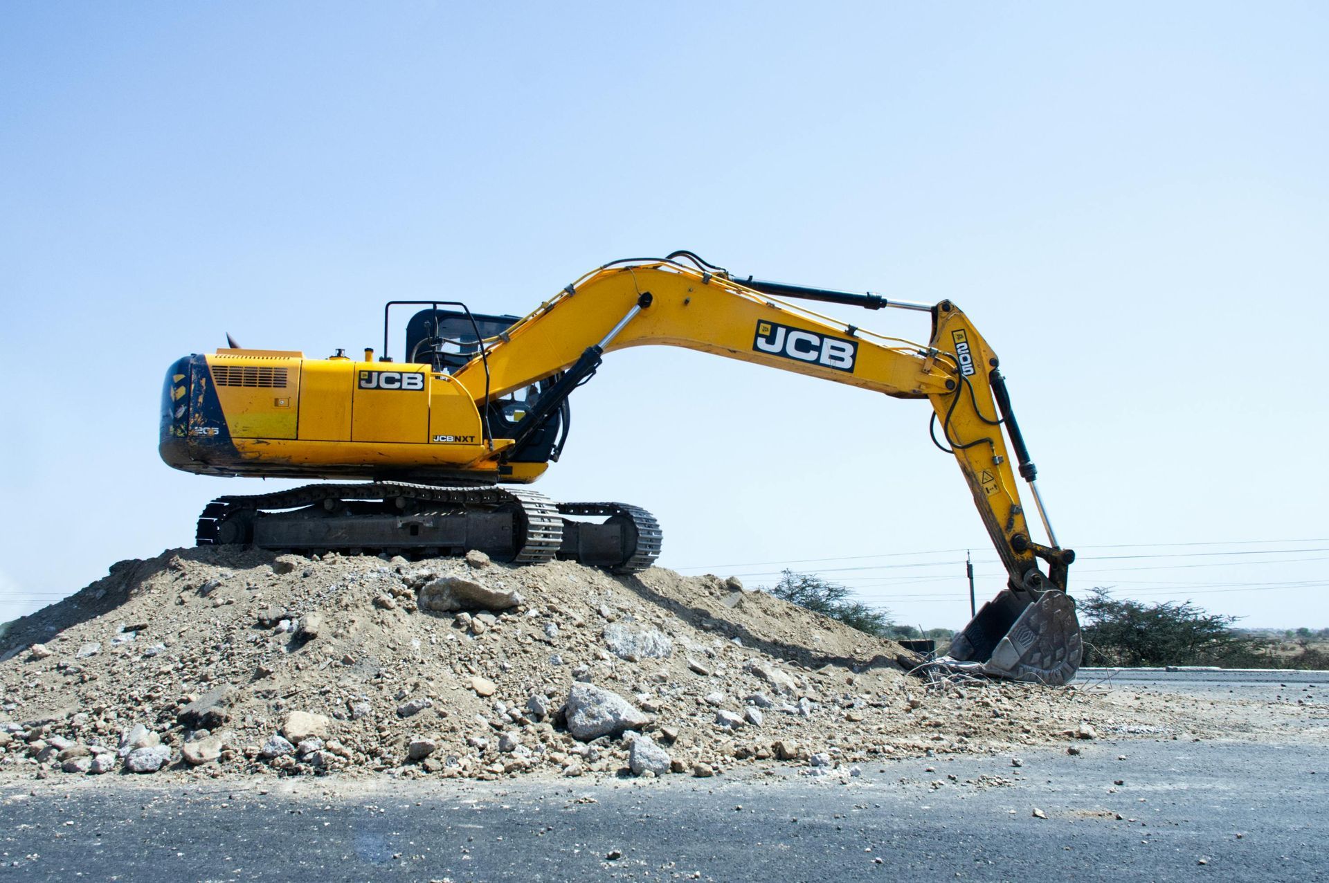 Yellow JCB excavator on a pile of dirt, poised to dig, set against a clear blue sky.
