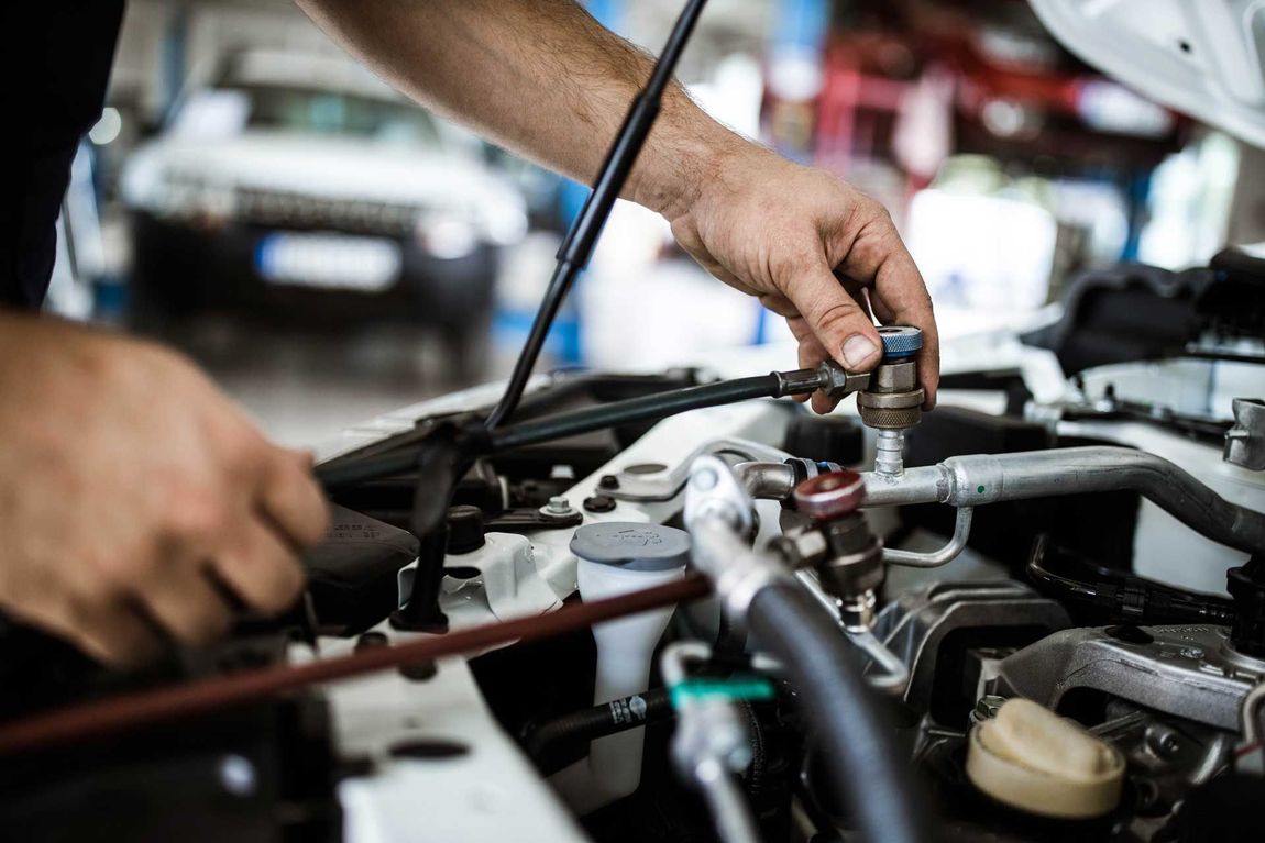 Mechanic’s hands working under an open car hood with tools in a repair shop