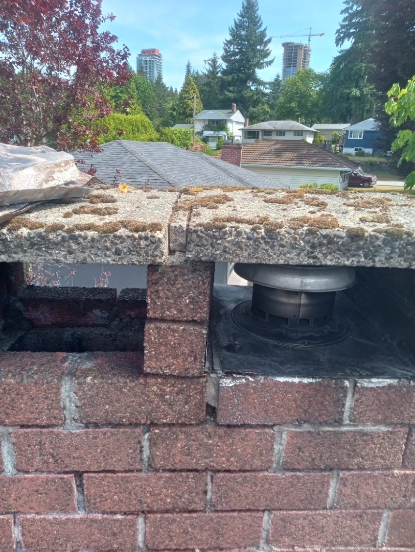 A close up of a brick chimney with a roof in the background.