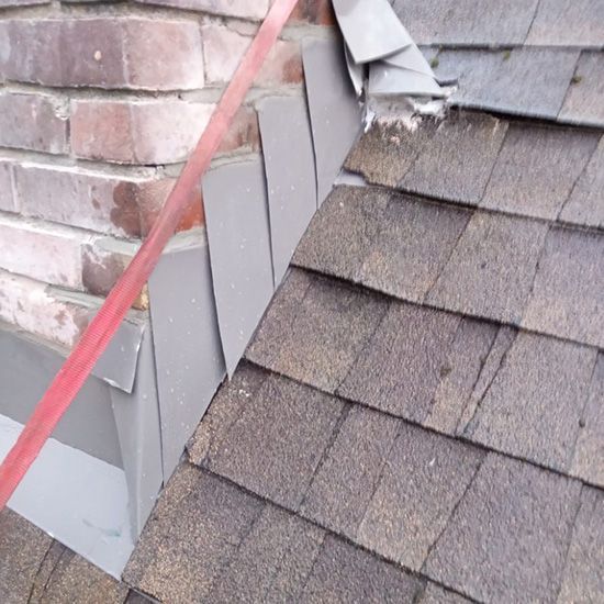 A close up of a roof with a brick chimney in the background