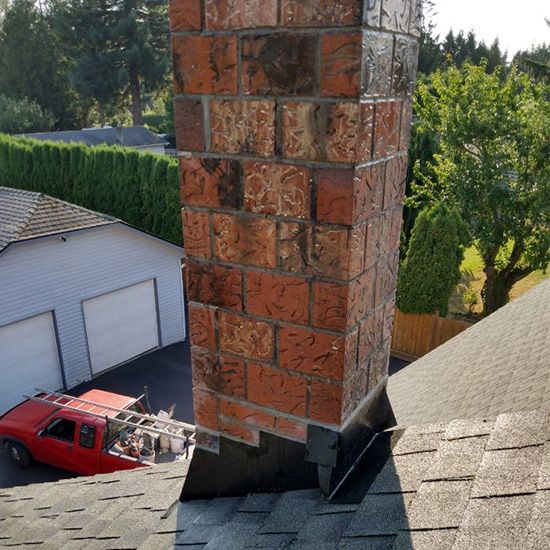 A brick chimney is sitting on top of a roof next to a garage.