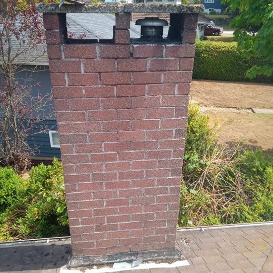 A brick chimney is sitting on a sidewalk in front of a house.