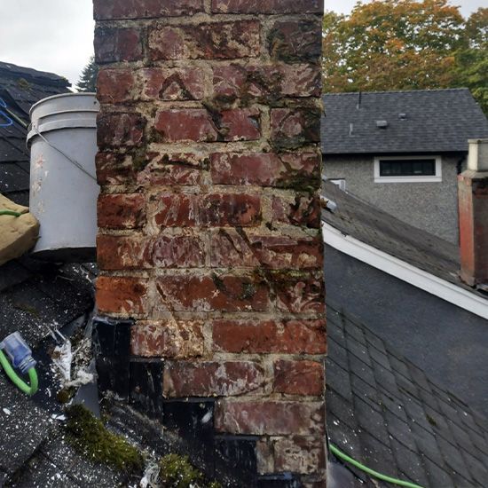 A brick chimney on top of a roof next to a bucket