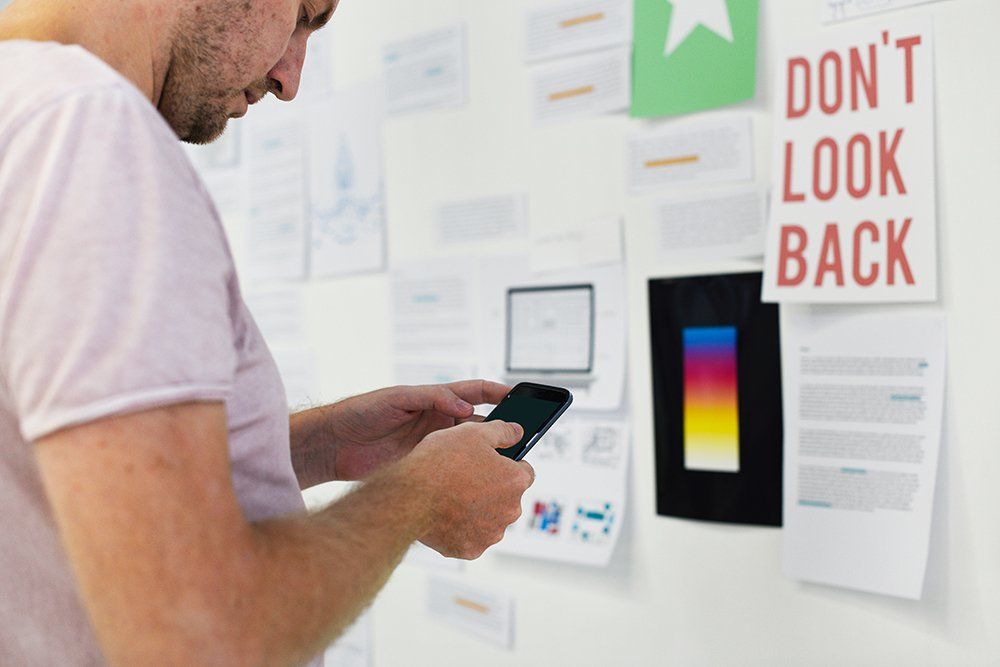 A man is using a cell phone in front of a white board with a sign that says do n't look back.