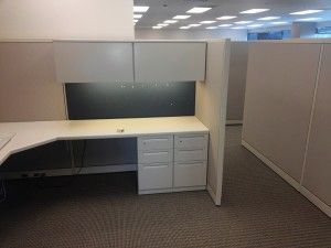 An empty cubicle in an office with a desk and drawers.