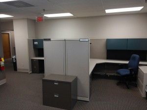 An empty office with cubicles , a desk , a chair and a filing cabinet.