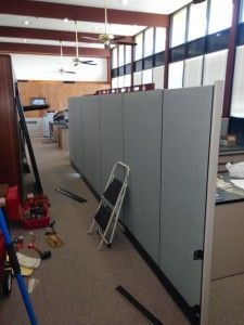 A ladder is sitting on the floor next to a cubicle wall.
