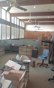 An empty office with a ceiling fan and a lot of boxes on the floor.