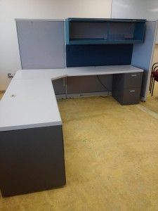 A cubicle with a desk , filing cabinet , and shelves.