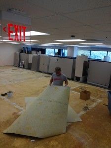 A man is holding a piece of carpet in front of an exit sign.