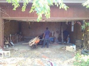 A man is standing in a garage with a wheelbarrow full of wood.