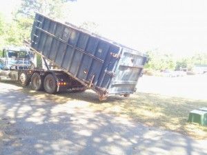 A dumpster is sitting on the side of the road next to a truck.