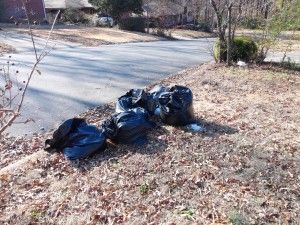 A bunch of trash bags are laying on the ground near a road