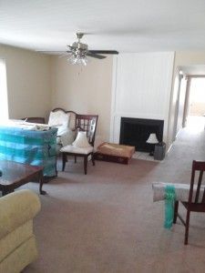 A living room with a fireplace , chairs , a table and a ceiling fan.