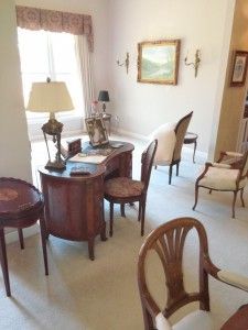 A living room with a desk , chairs , tables and a lamp.