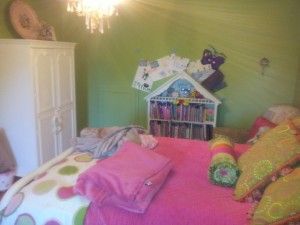 A girl 's bedroom with a pink bed and a doll house on the wall.
