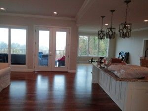 A living room with hardwood floors and a kitchen with a lot of windows.