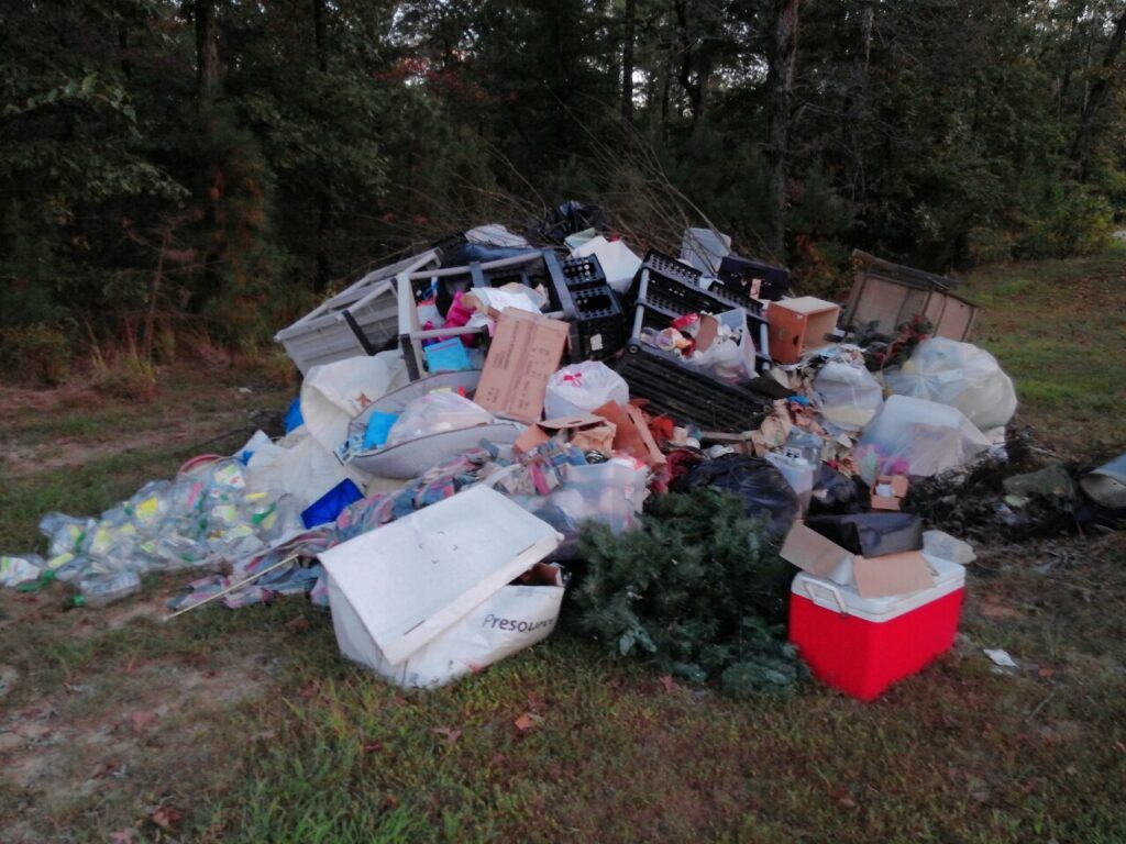 A pile of trash is sitting in the grass next to a red cooler.