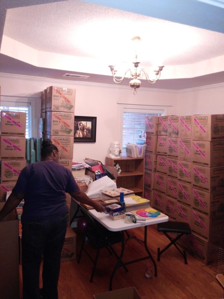 A woman is standing in a room filled with boxes and a table
