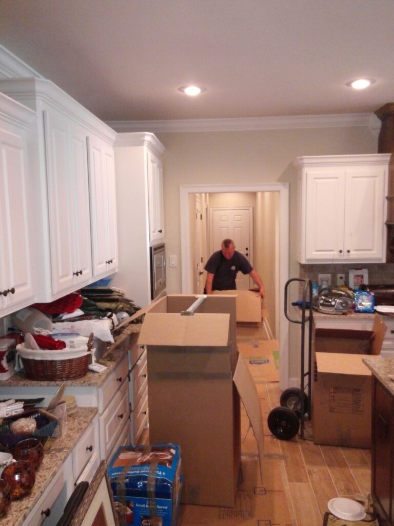 A man is standing in a kitchen surrounded by cardboard boxes