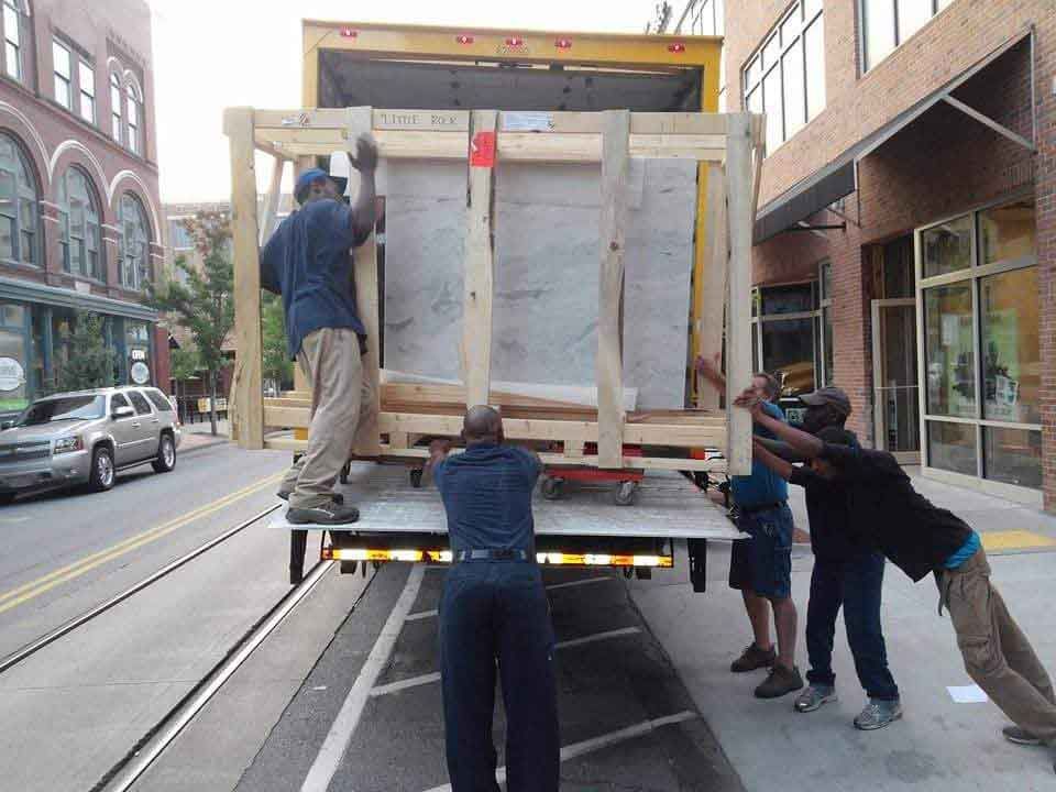A group of men are pushing a large wooden box on the back of a truck