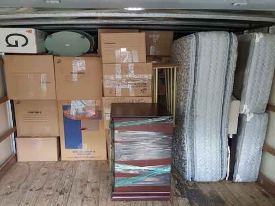 A truck filled with boxes , mattresses , and a dresser.