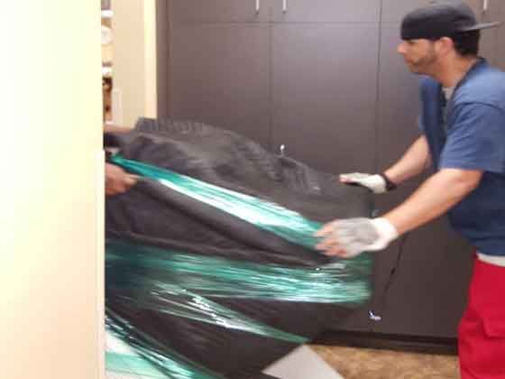 A man is wrapping a large black object in plastic wrap.