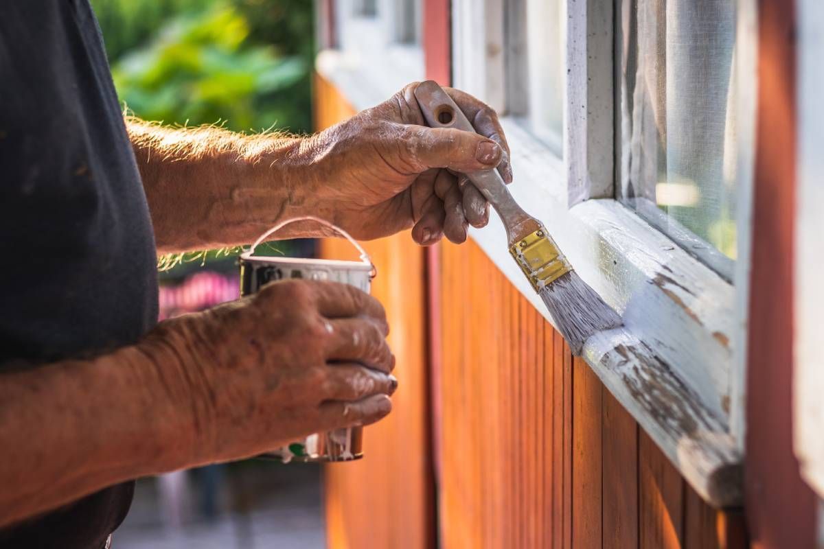 Someone applying fresh Benjamin Moore paint to a cabin window frame at John Paul's Paint and Decor near Bourbonnais, Illinois