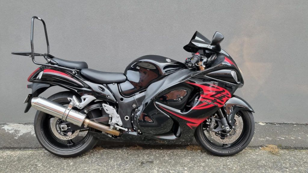 A black and red Suzuki Hayabusa sport bike parked against a gray wall, featuring an attached rear passenger backrest.