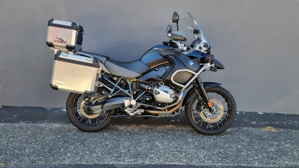A dark blue BMW adventure motorcycle with silver hard-shell panniers and a top case parked against a plain wall.