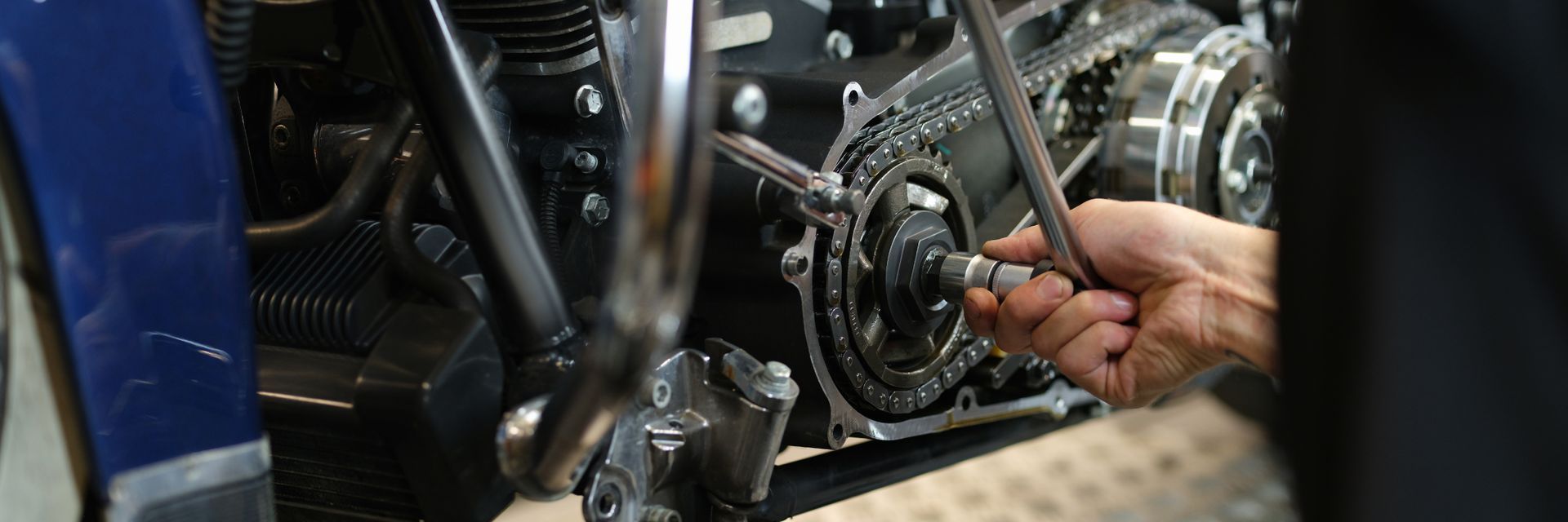 A close-up of a hand using a wrench to adjust the chain-driven engine components on a motorcycle.