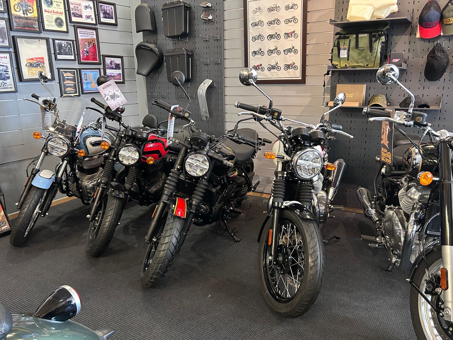 A row of parked motorcycles inside a showroom with framed pictures on the wall and accessories displayed on a pegboard.
