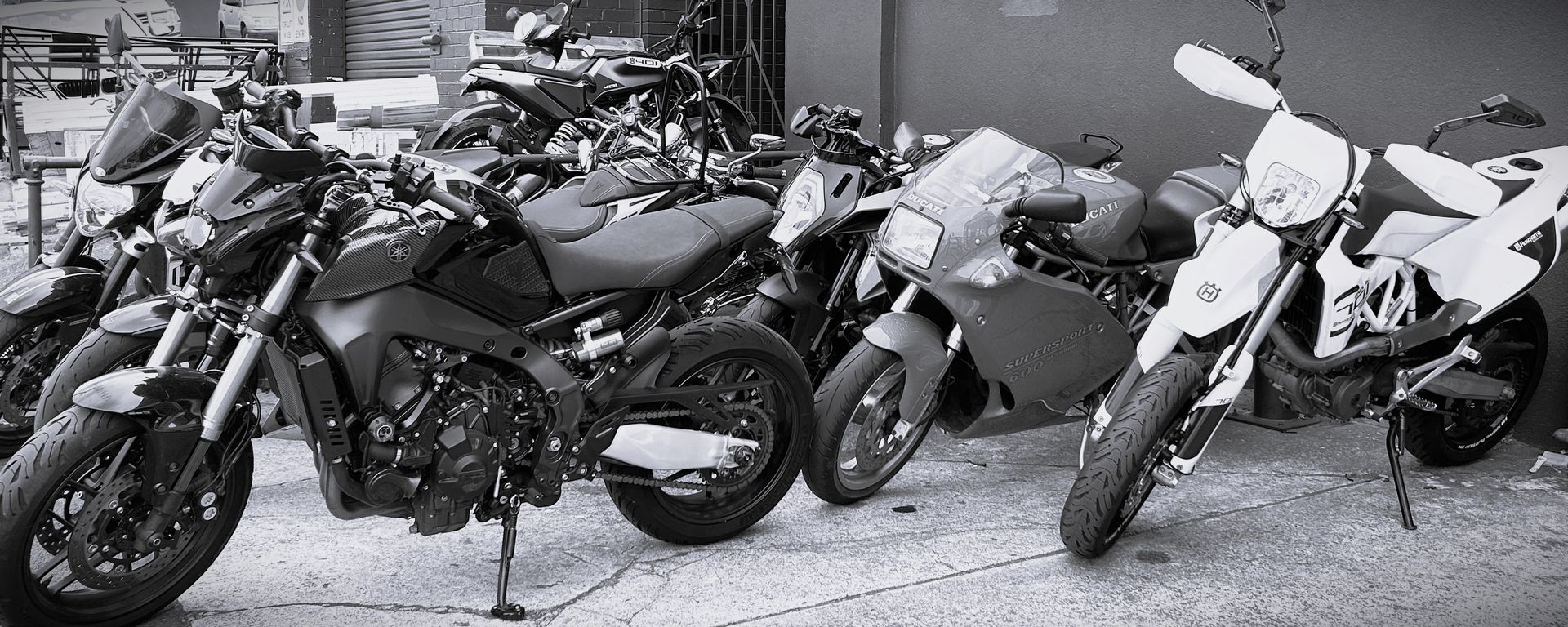 Row of parked motorcycles lined up on a street, shown in black and white