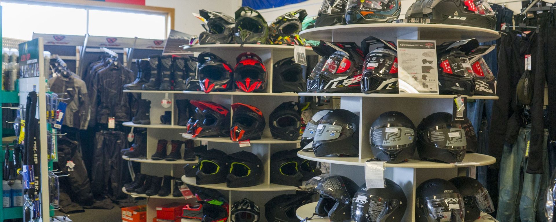 A retail store interior showing circular displays filled with various motorcycle helmets and riding boots on shelves. A retail store interior showing circular displays filled with various motorcycle helmets and riding boots on shelves.
