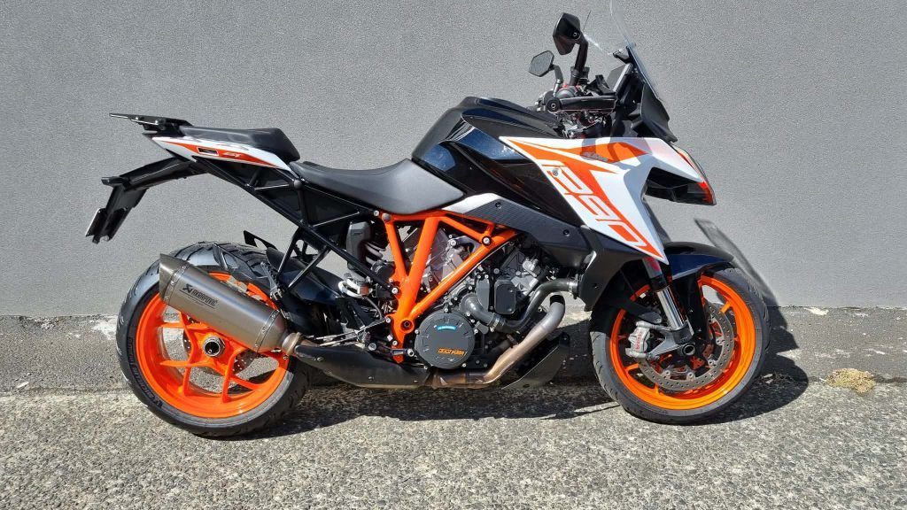 A KTM 1290 Super Duke GT sport-touring motorcycle with a black, white, and orange color scheme parked on gravel.