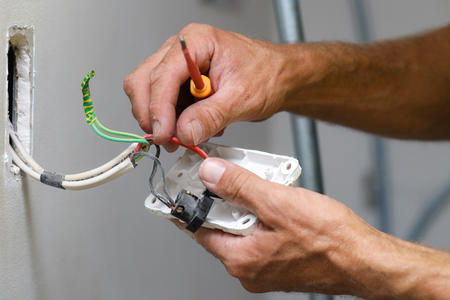 A Electrician Working With Wires and a Screwdriver Inside a Wall Outlet Box — McGrath Electrical & Data in South Grafton, NSW