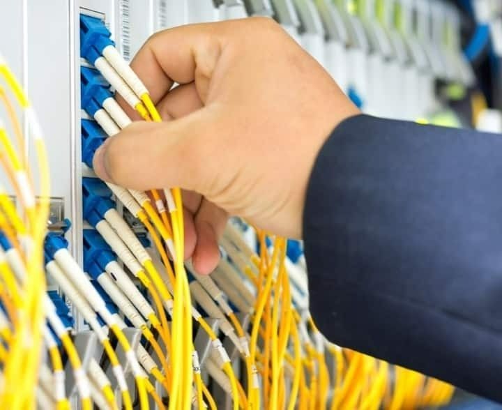 A Person's Hand Connecting Yellow Fiber Optic Cables — McGrath Electrical & Data in South Grafton, NSW