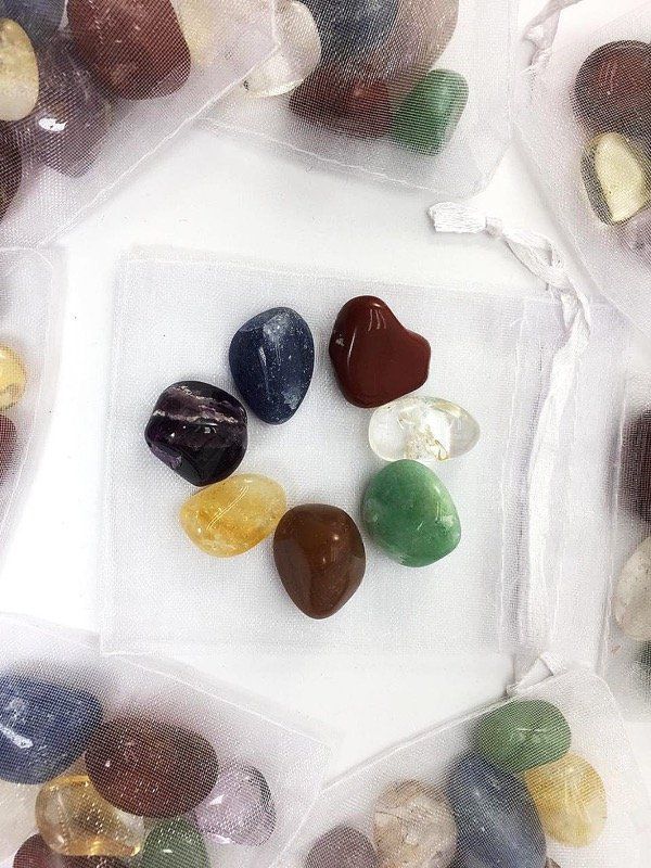 Siete piedras rodadas de colores dispuestas alrededor de una bolsa blanca con cordón.