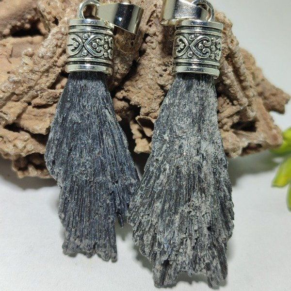 Colgante de cianita negra con casquillo de plata, que reposa sobre una superficie marrón texturizada.