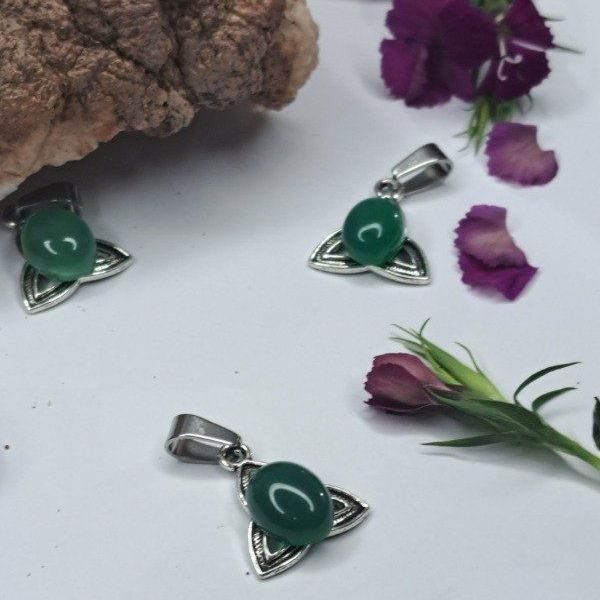 Colgantes de nudo celta plateados y verdes dispuestos con flores sobre una roca.