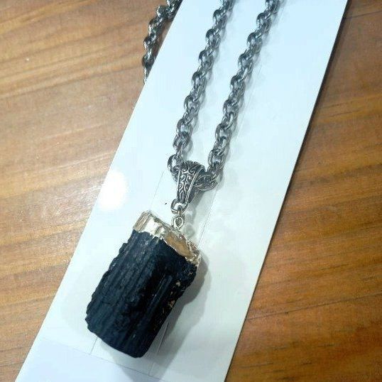 Colgante de turmalina negra en una cadena de plata, con bordes dorados, sobre una tarjeta blanca.