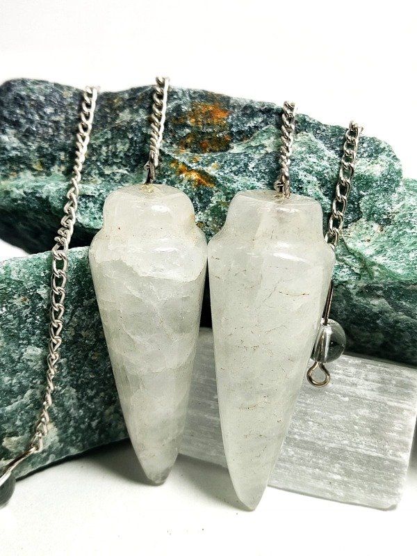 Péndulo de cristal blanco con cadena de plata sobre un fondo de roca verde texturizada.