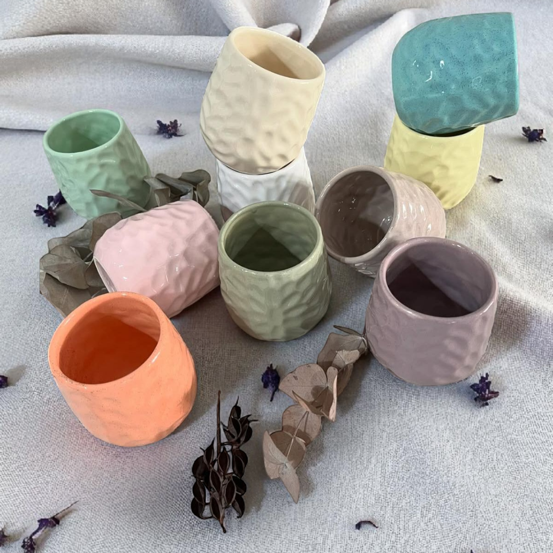 Seis tazas de cerámica en varios colores pastel con exteriores texturizados, colocadas sobre una mesa con lavanda.