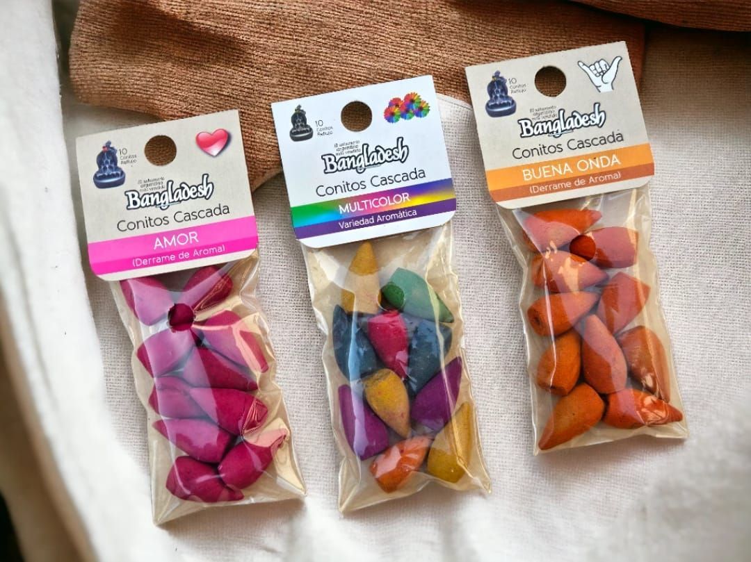 Siete coloridos conos de incienso en envase transparente, dispuestos sobre una superficie de madera con flores amarillas.