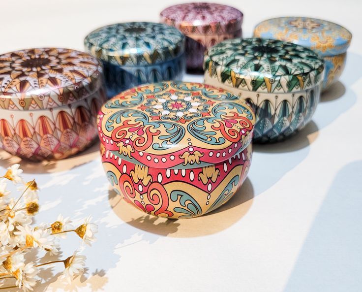 Seis velas redondas con diseños en varios colores, sobre una superficie rosa.