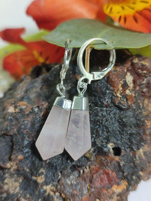 Pendientes de cuarzo rosa con ganchos plateados sobre un fondo oscuro texturizado.