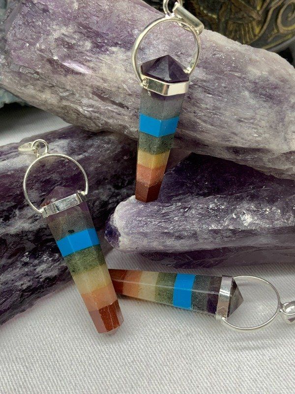 Primer plano de colgantes de piedras preciosas de colores con aros de plata, sobre cristales de amatista púrpura.