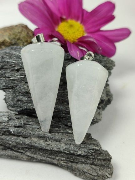 Dos péndulos de cristal blanco, una flor rosa y una piedra gris sobre fondo blanco.