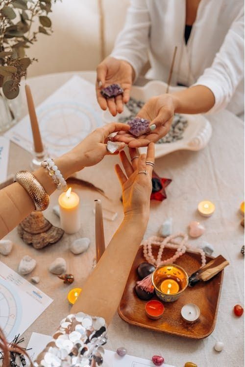 Manos compartiendo cristales de amatista alrededor de una mesa con velas, piedras y una carta astral. Un ambiente espiritual.
